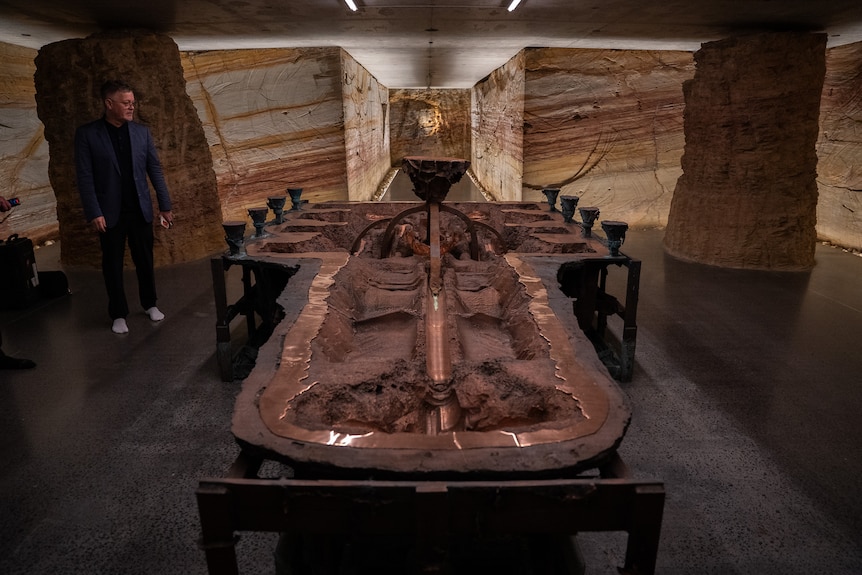 A man looks on at a massive bronze sculpture sitting in the tunnels of the Mona library.