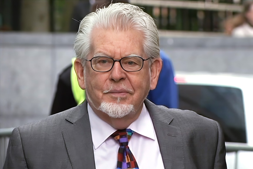 Rolf Harris in a grey suit walking into court