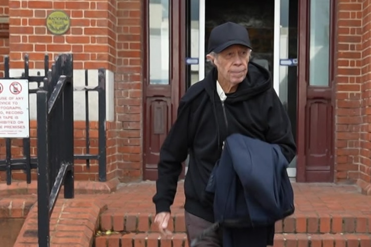 A man in a black jacket and cap is walking along a red brick path.