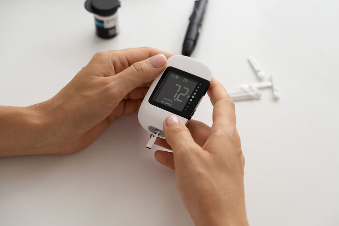 Hands holding a blood glucose meter, showing a reading, highlighting medical aspects of care for patients by nurses.