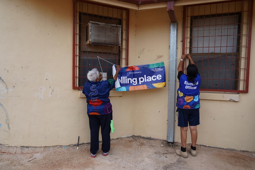 Two women put 'polling booth' sign up on wall