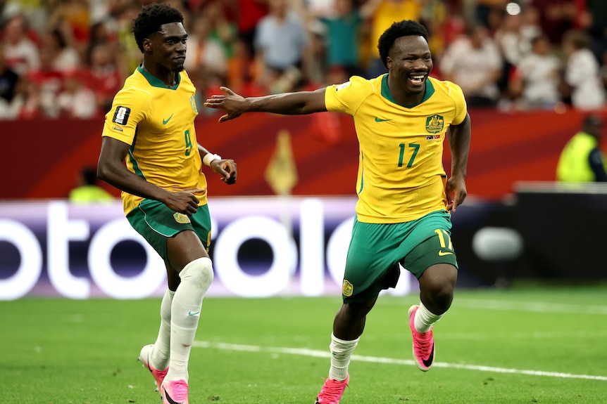 Two soccer players in green and gold celebrate a goal