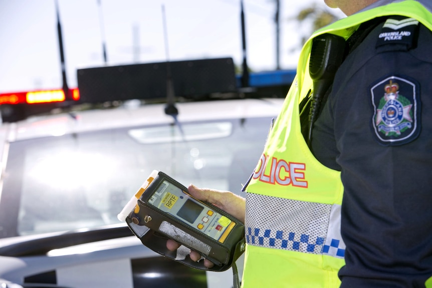 A police officer in uniform and high-vis vest holding an rbt unit.