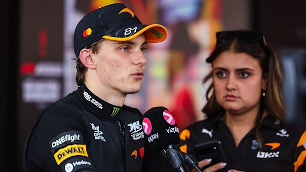 A Formula 1 driver speaks in front of microphones.