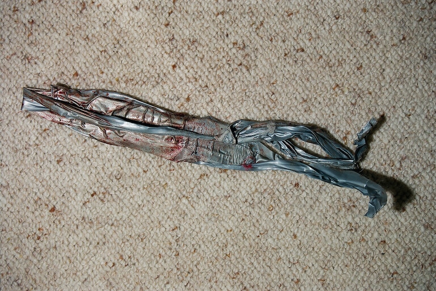 A strip of grey, bloody duct tape sitting on beige carpet.