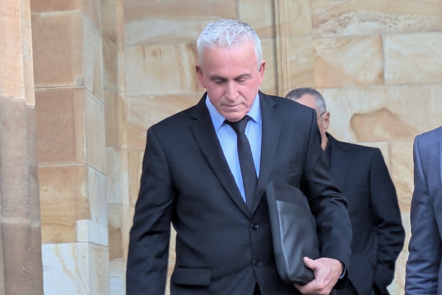 A man in a suit is holding a black zip-up folder.