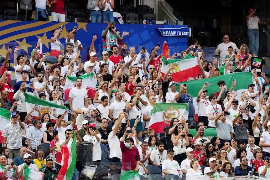 A section of Iran fans inside the stands, waving Lion and Sun flags