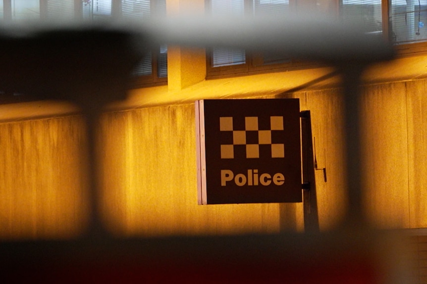 A police sign with the checker symbol of police on the side of a building at night.