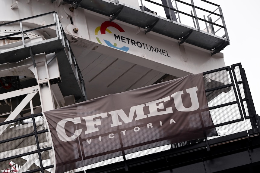 A black sign with 'CFMEU Victoria' written on it, hanging on a construction site.