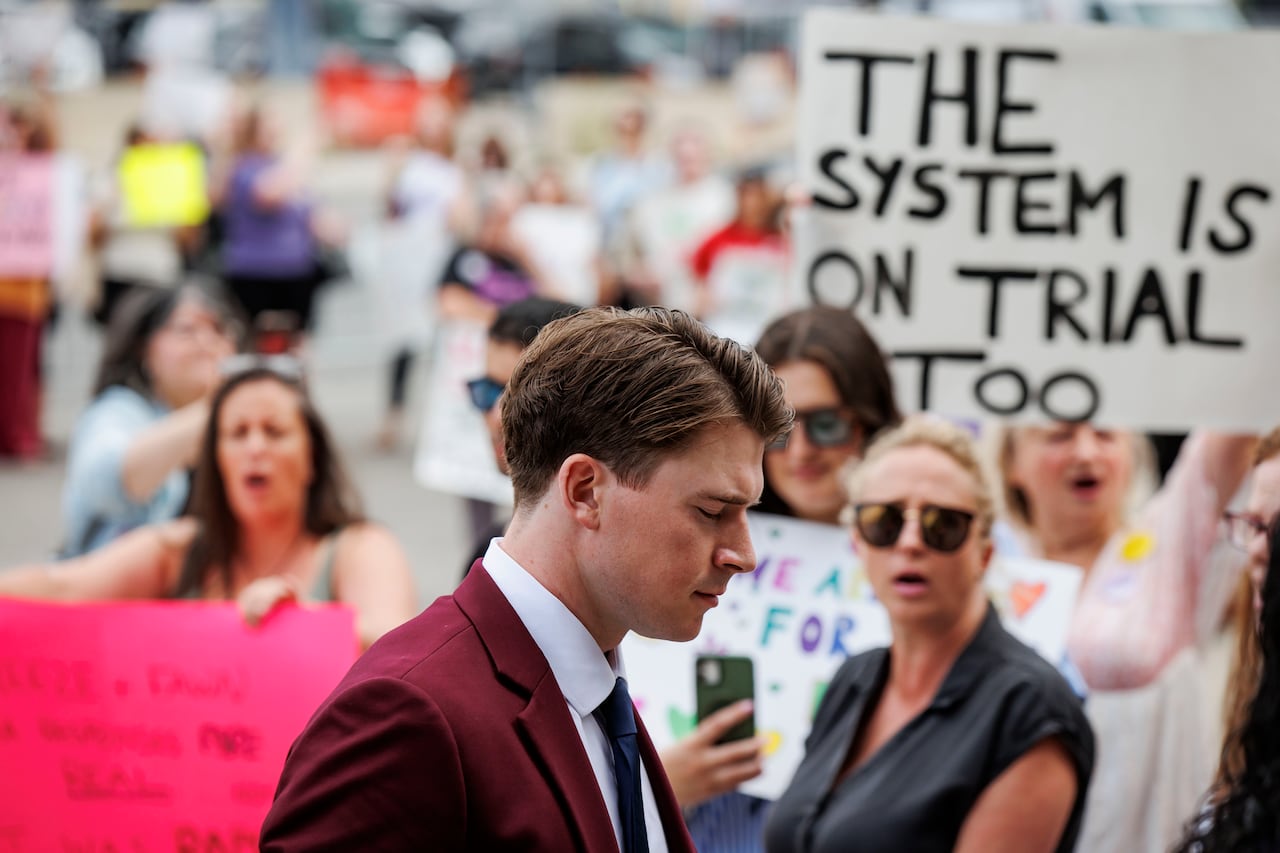 man walking to court past women carrying signs