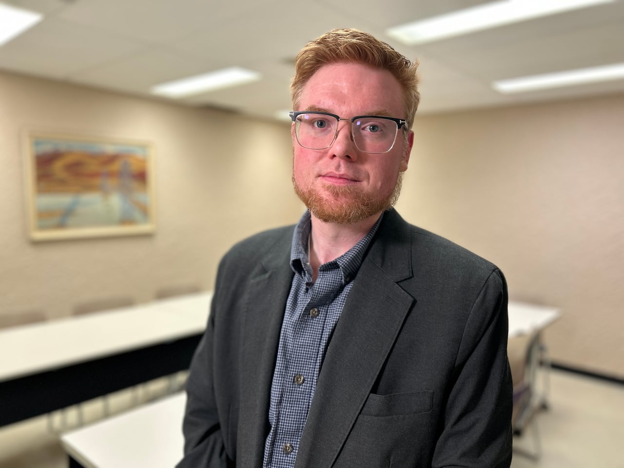 A man with short, red hair and close-cropped beard, wearing a dark blazer and glasses.