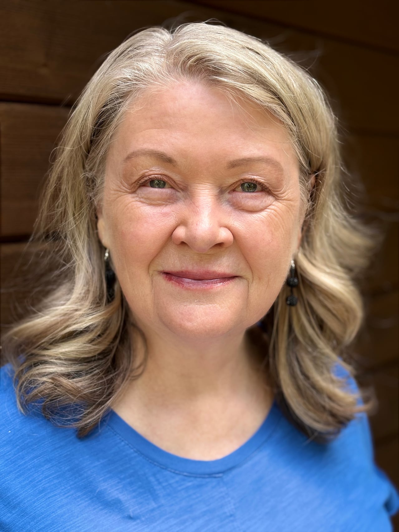 A woman with shoulder length blond hair is smiling. She's wearing a blue shirt.
