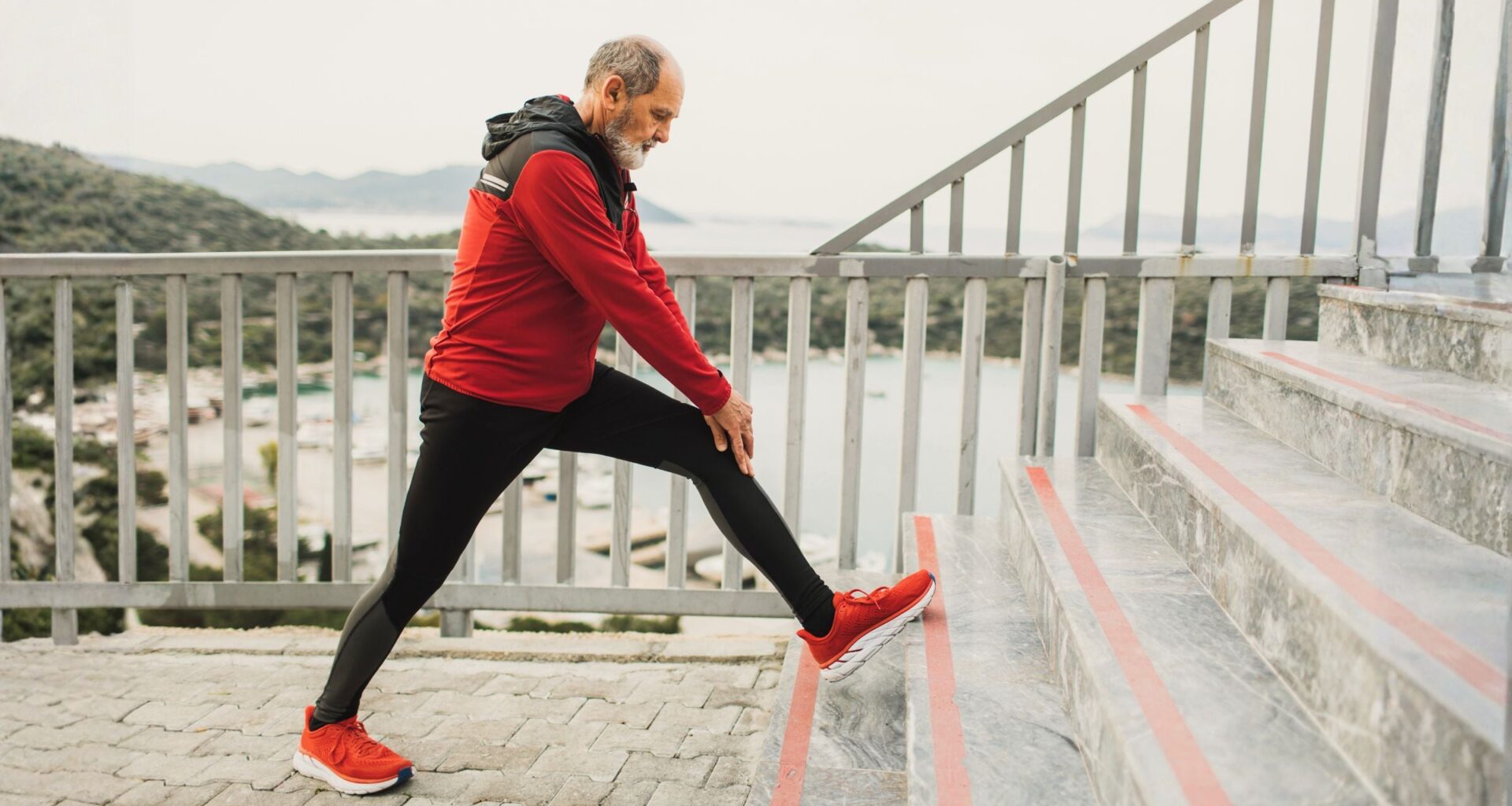 Senior man warming up body and legs in morning before jogging. Healthy lifestyle in old age. Active grey-haired senior on retirement.