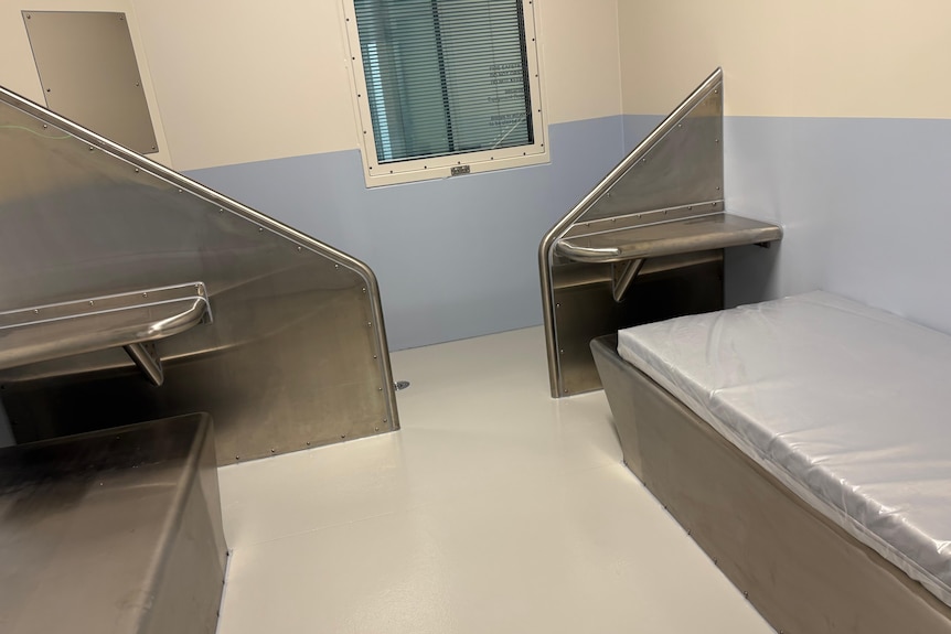 A detention cell with a mattress and metal bench.