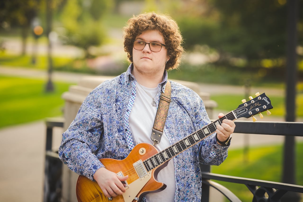 A man in a shirt outside holding a guitar