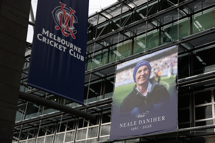 A billboard on the outside of a sports stadium showing a smiling man wearing a blue beanie and the words "Neale Daniher".