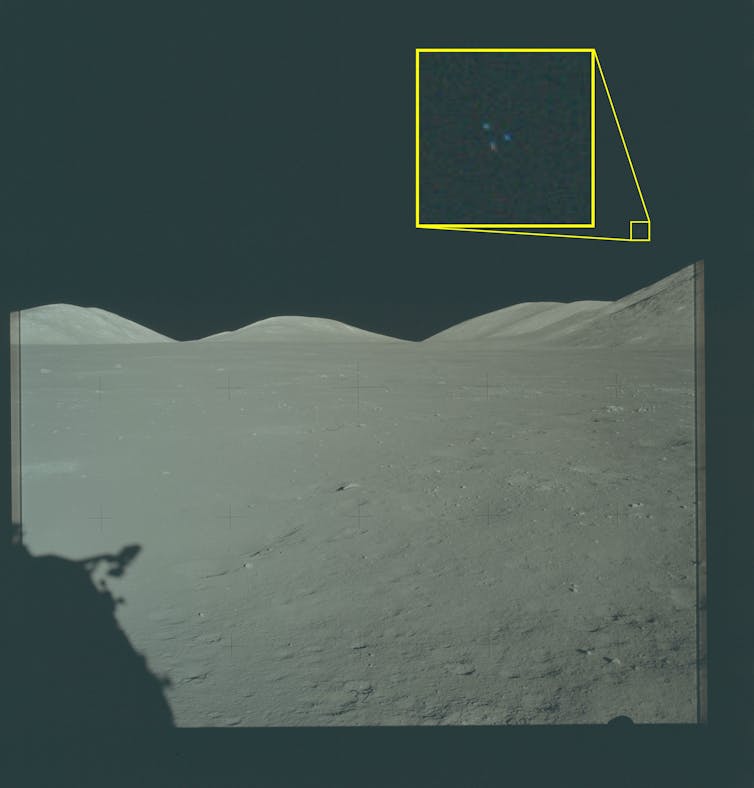 A grey, lunar surface with three colourful dots visible in the sky.