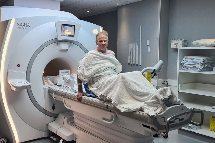 Richard Scolyer in hospital gown sitting up in an MRI scan room