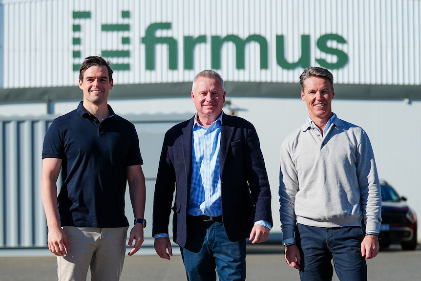 Three men standing outside a building that says 'Firmus'.