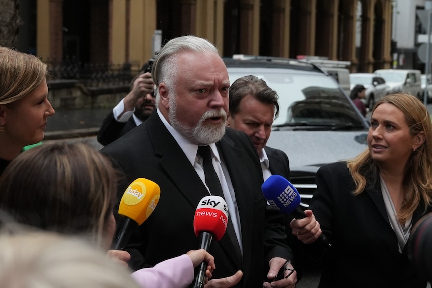 Mr Sandilands wearing a suit talking to reporters outside court.