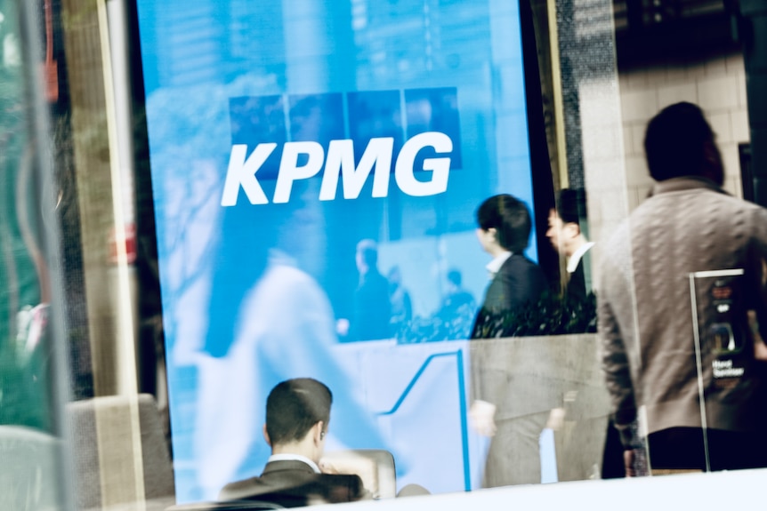 Office workers near a window with KPMG printed on it.