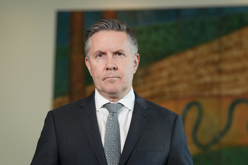 A man in a navy suit and tie looks sternly into camera.