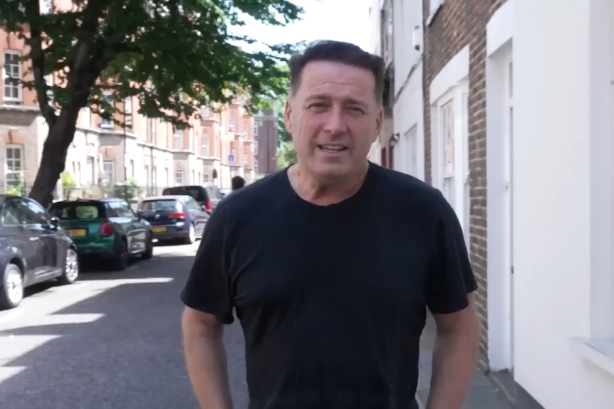 A man in a black tshirt stands on an inner-city London street.