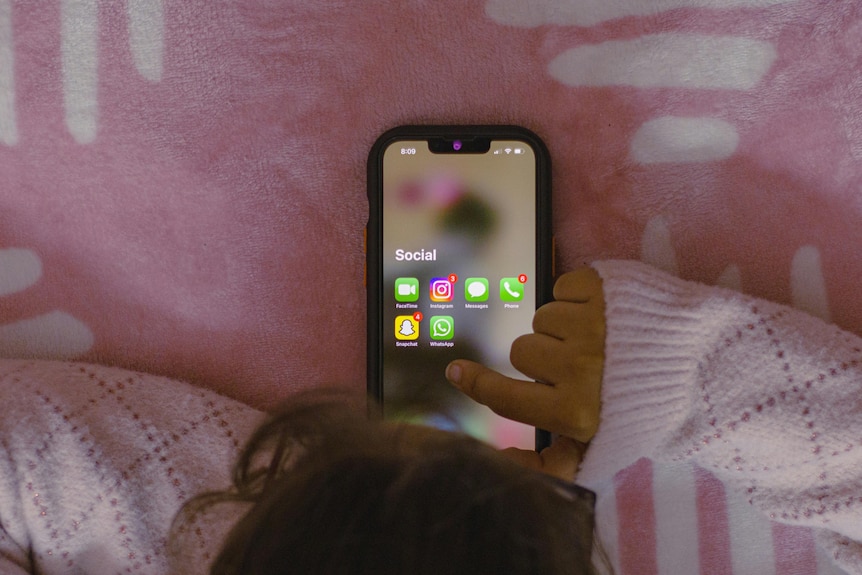Seen from above, a young girl browses a folder of social media apps on a phone