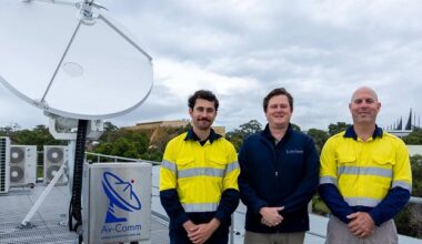 Three men standing next to a satellite dish installed on a rooftop