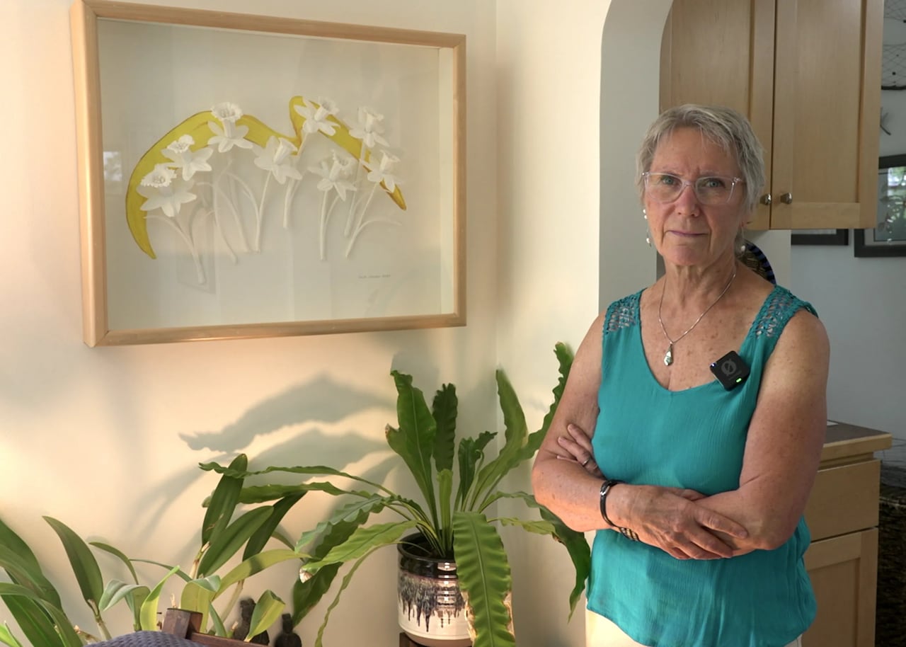 A woman in a blue tank poses in front of a white and yellow art piece.