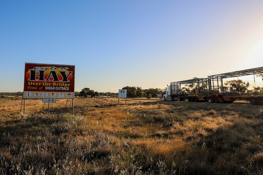 A sign that reads Explore Hay stands by the roadside as a truck passes at sunrise