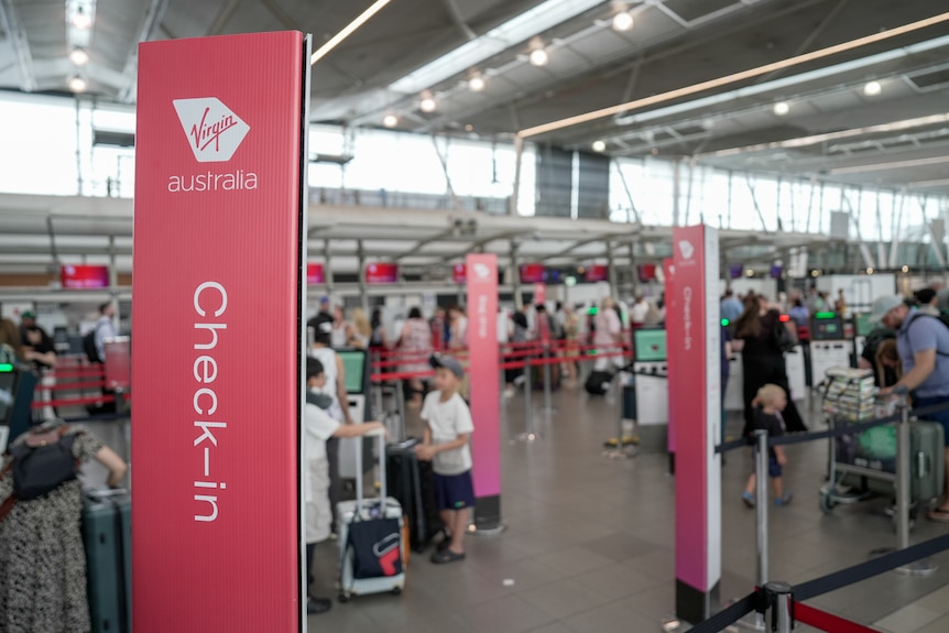A Virgin check in sign with people lined up in the background.