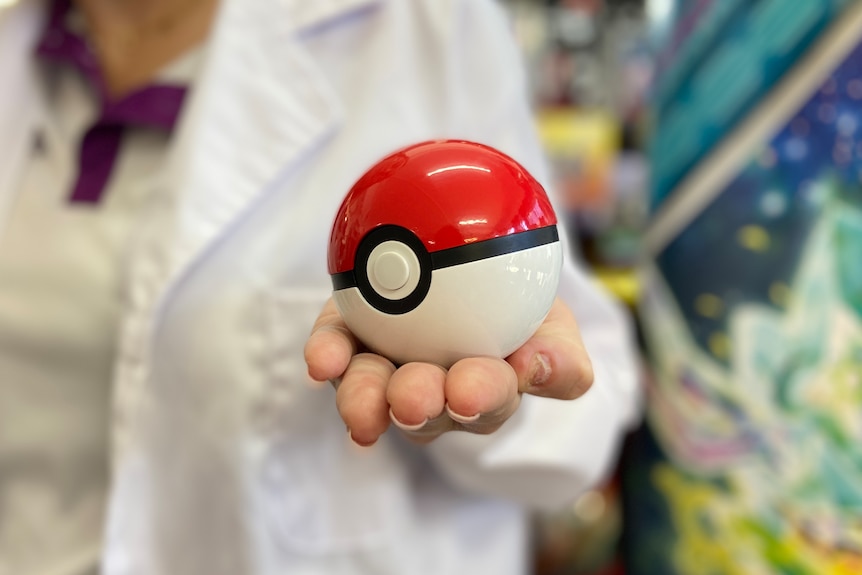 A close up of a woman in a white coat holding out a half red, half white ball.