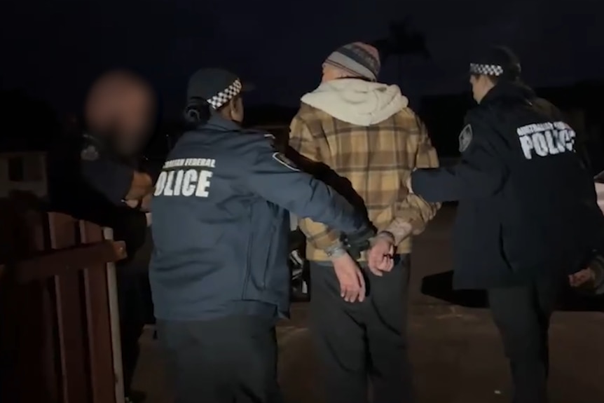 Man wearing beanie being escorted by AFP officers