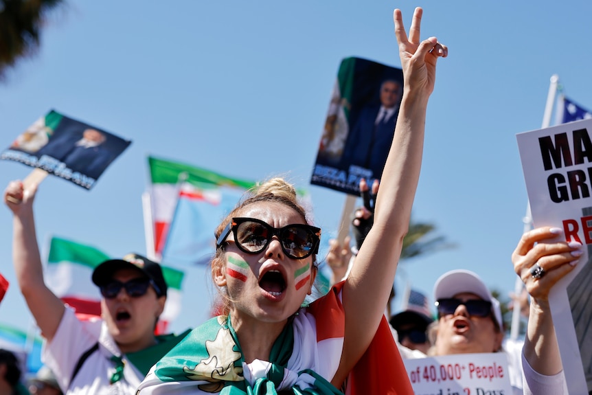 A protester draped in an Iranian flag holds her fingers up