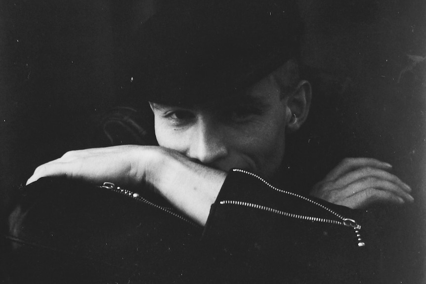 Black and white photo of a young Jerry Coleby-Williams wearing a black flat cap and half hiding behind his arms