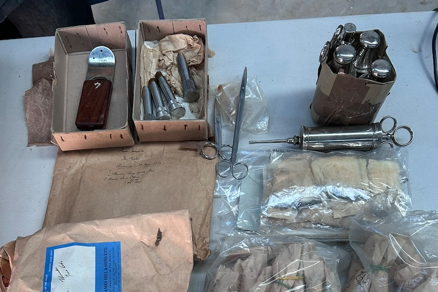Several boxes on a table filled with old metal syringes, scissors and small bags of wool.
