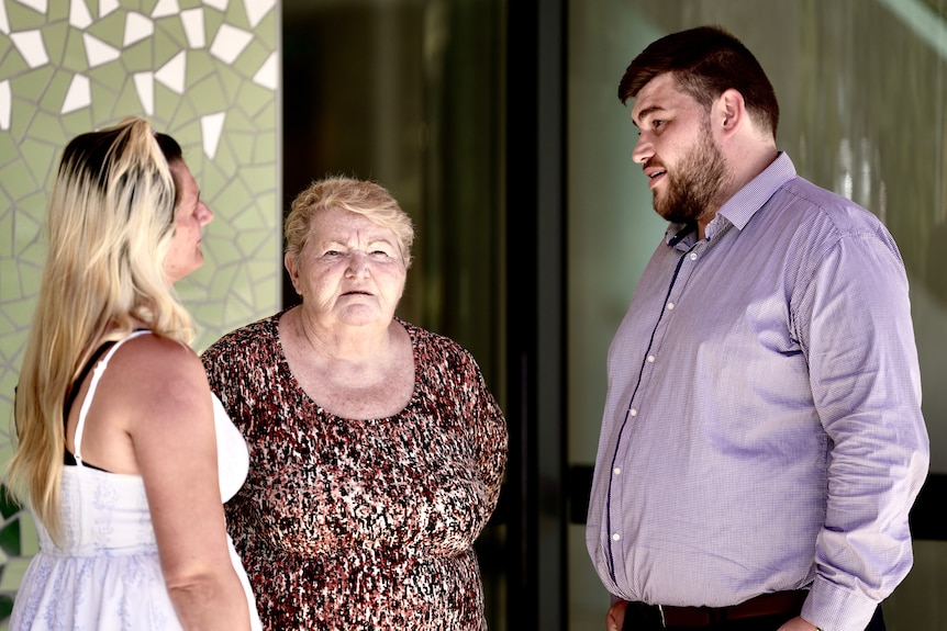 Two women and a man stand together outside a building.