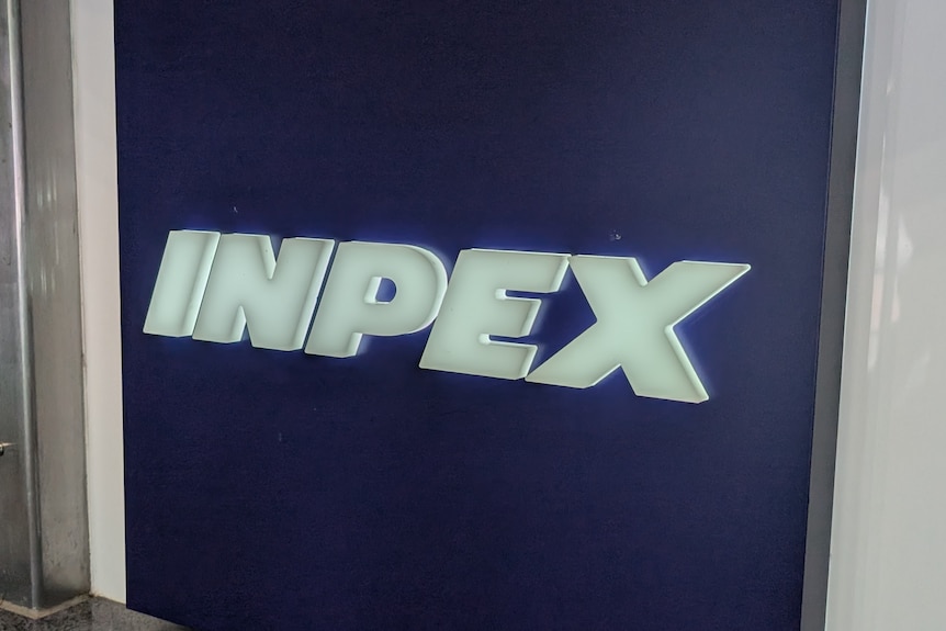 A sign in an office reads INPEX, the text is white block letters on a navy blue background.