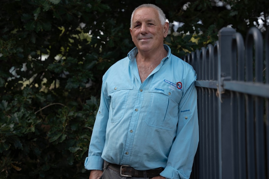 A man stands by a fence smiling at the camera.