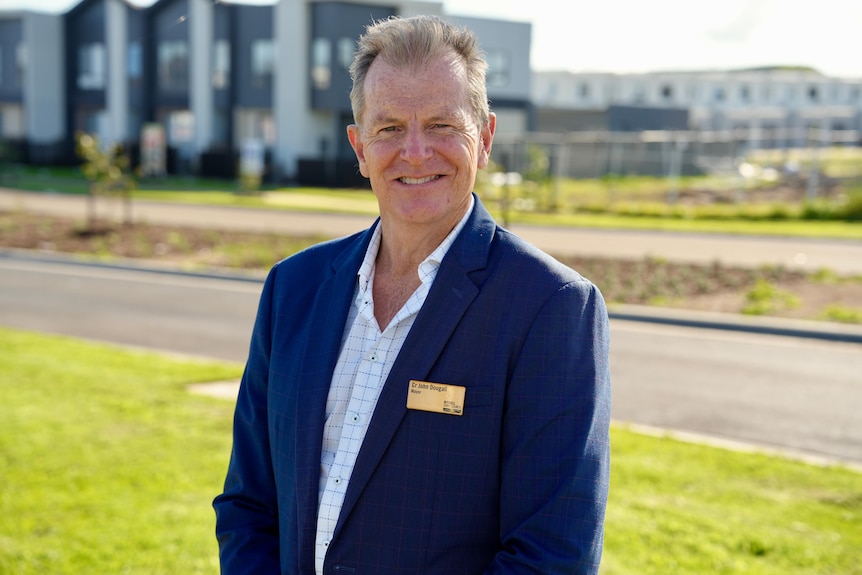 Man in blue blazer stands in front of suburban development