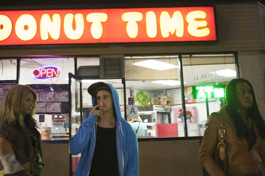 Three people stand in front of a shop called Donut Time
