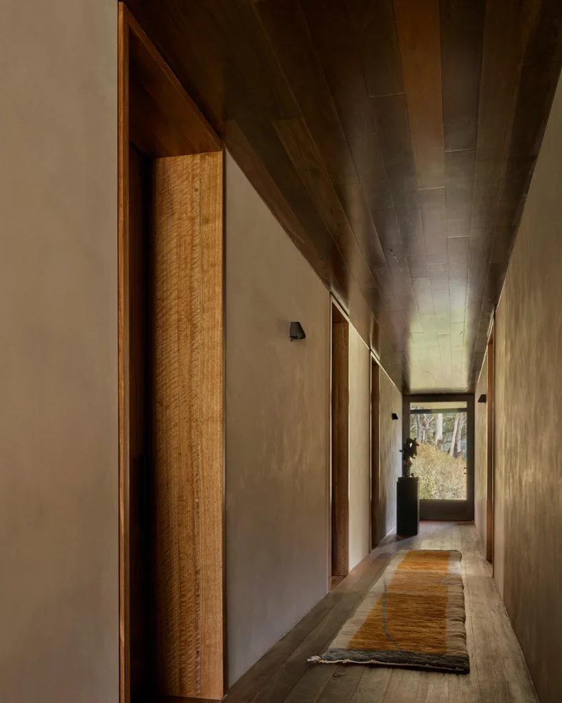 A brutalist hallway with a window at rear framing views, grounded by a runner.