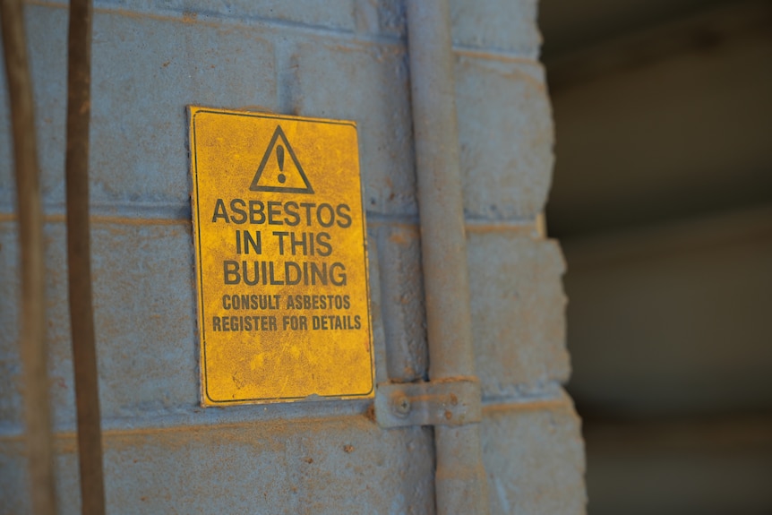 A yellow sign reading Asbetos on a grey wall