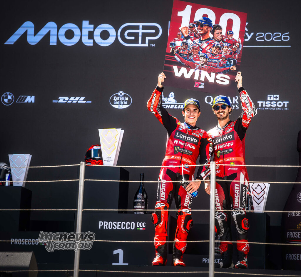 Marc Marquez and Francesco Bagnaia hold a Ducati 100 wins board on the podium.