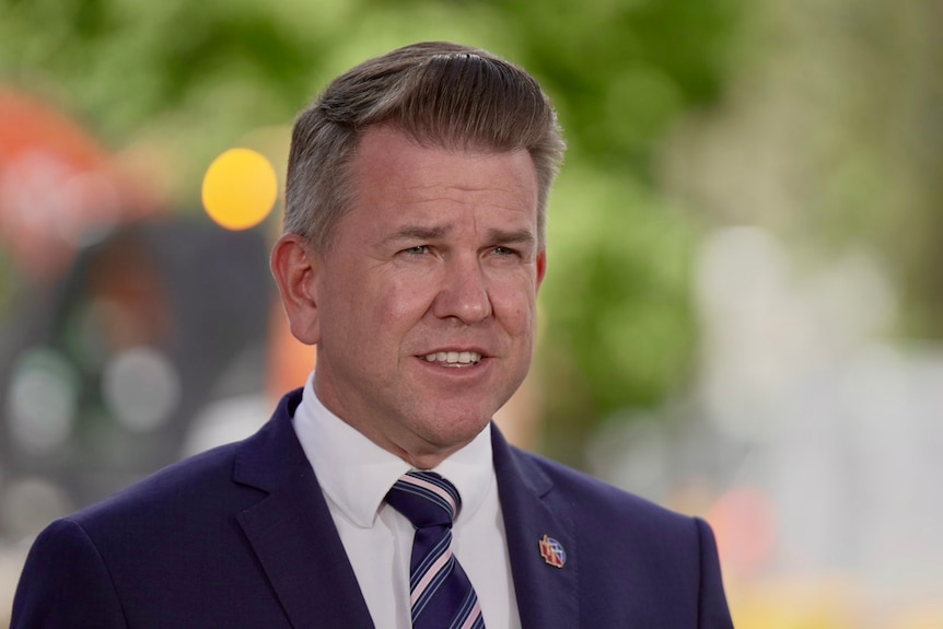 Jarrod Bleijie wearing a navy suit and navy and white tie speaks at a press conference.