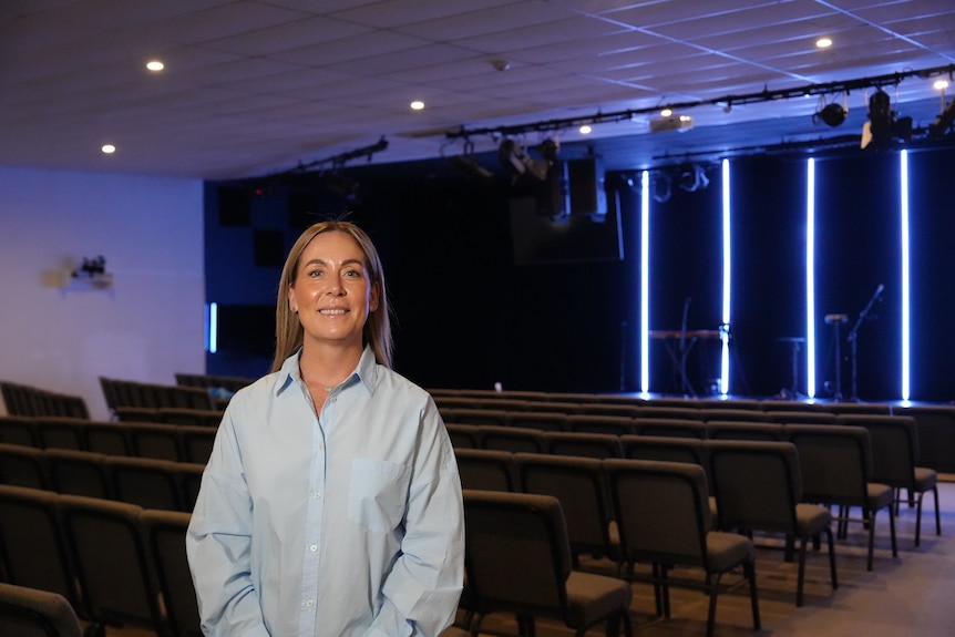 Jade Lewis stands in an auditorium while smiling and wearing a blue business shirt