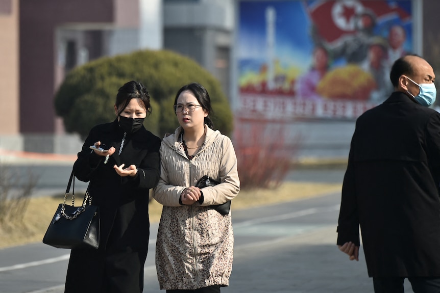 People walking along a North Korean street with a billboard in the background.