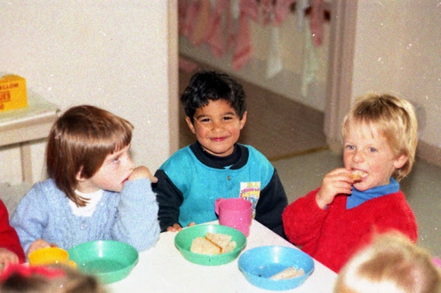 Marc, centre, sits in a classroom at the corner of a table between other children in the 90s.
