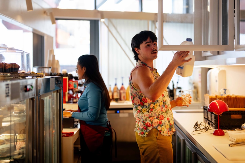 A woman takes someone's order whilst a man puts milk in a cupboard